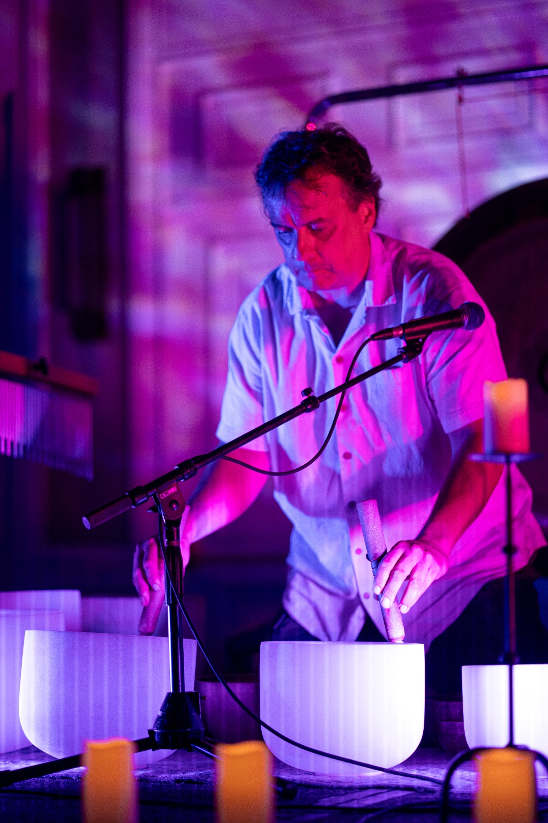 Guy Douglas playing crystal singing bowls in purple stage light