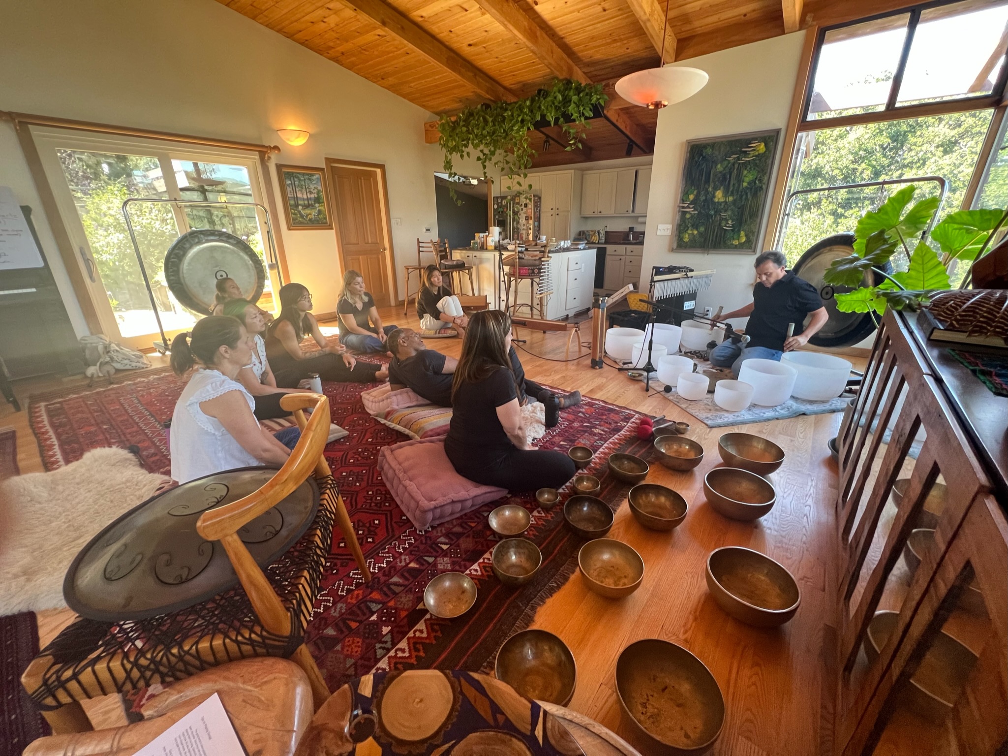 Guy demonstrating singing bowls to a circle of students in a wood-beamed training room