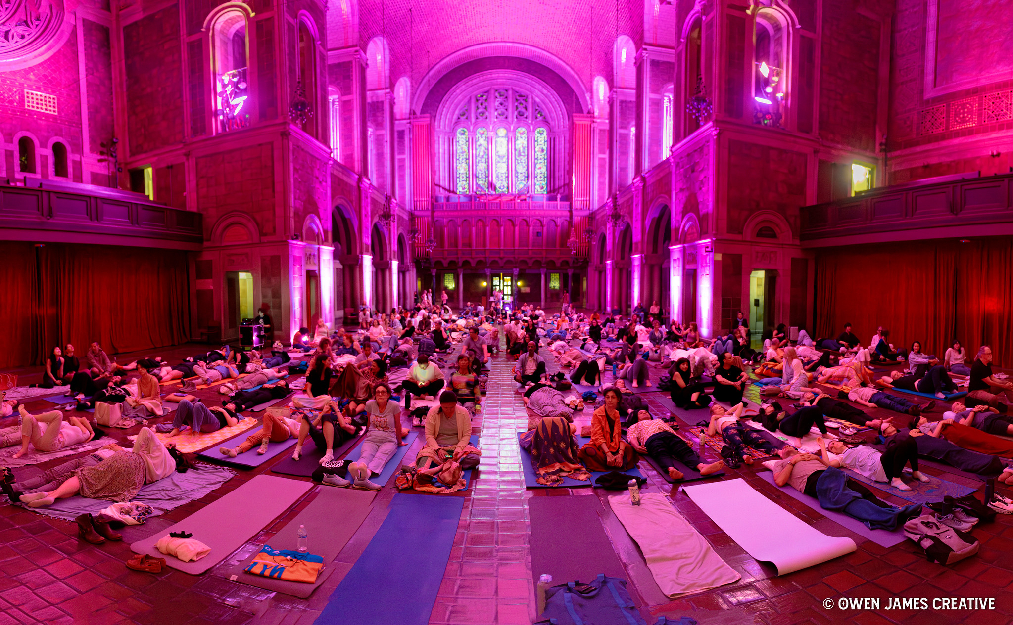 Hundreds of guests resting on mats at a sound bath inside a cathedral bathed in magenta light