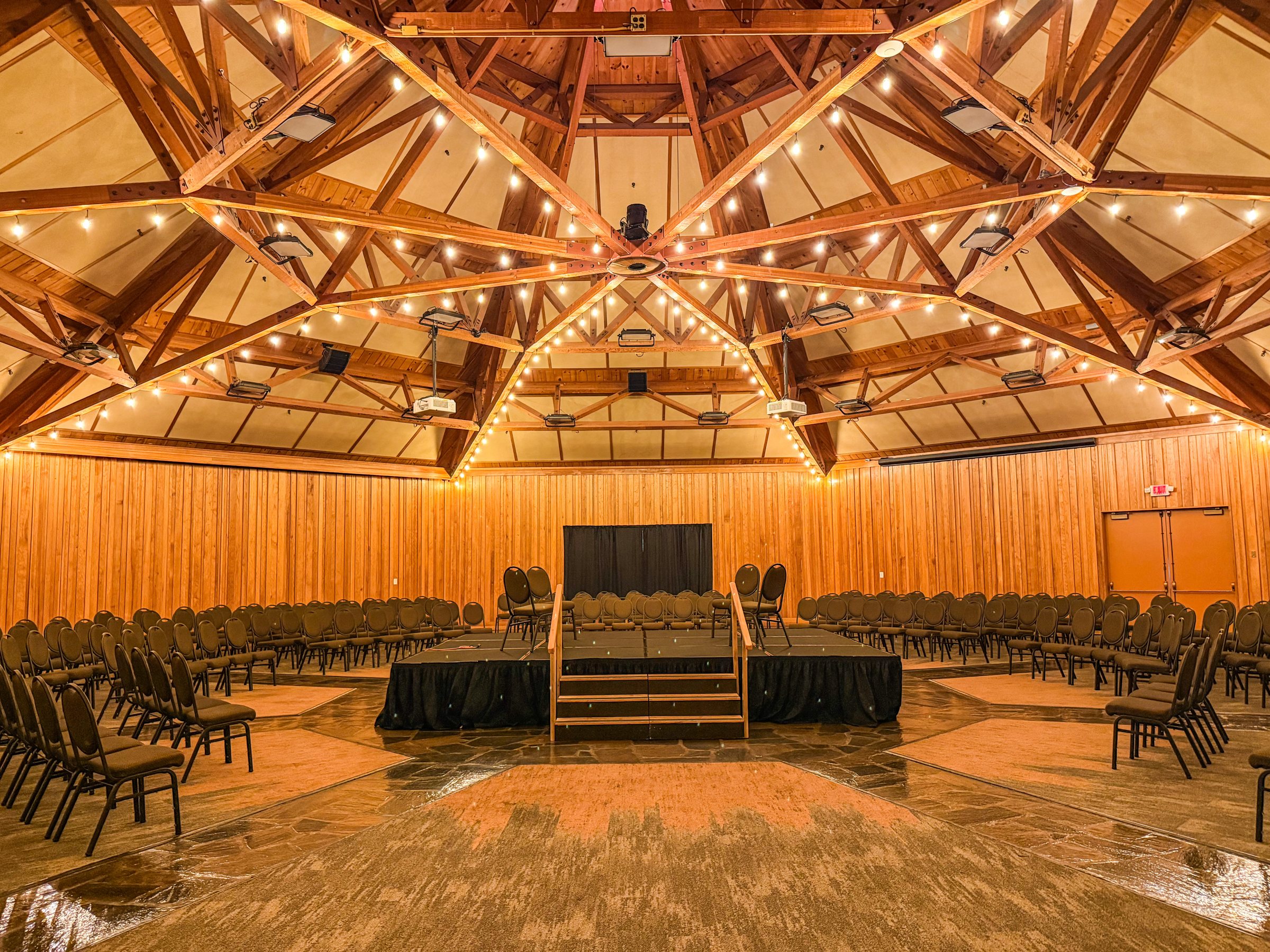 The timber-vaulted hall at the World Forestry Center in Portland, glowing with string lights above a stage and rows of chairs.